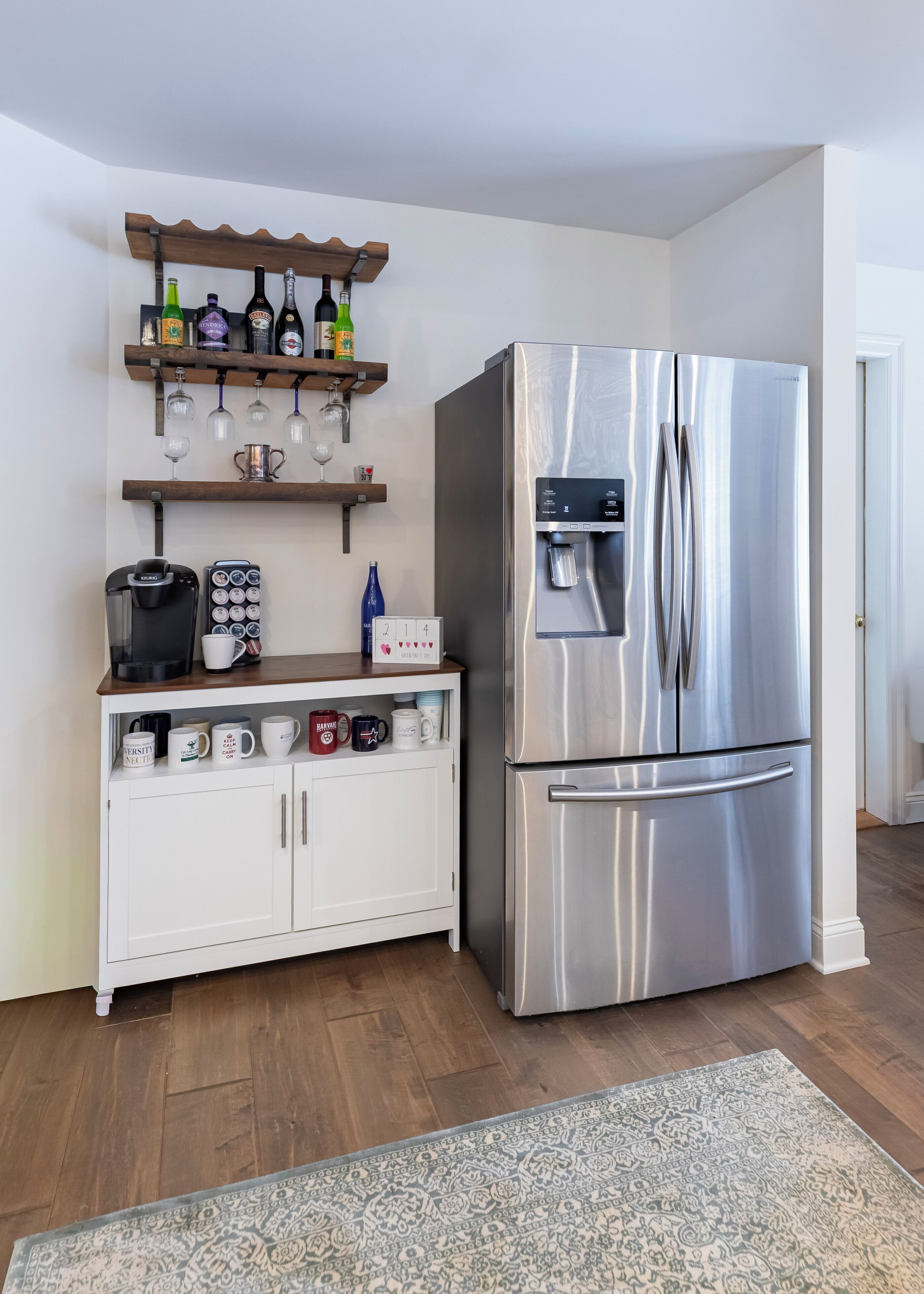 A modern kitchen with a stainless steel refrigerator, a coffee maker, and a shelf with various bottles and glasses.