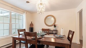 Een eetkamer met een houten tafel gedekt voor vier personen, omringd door stoelen. Een kroonluchter hangt aan het plafond en een grote spiegel aan de muur.