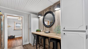 Une cuisine avec un plan de travail en bois, des tabourets de bar noirs, un miroir rond et un meuble blanc.