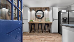 Une cuisine avec un plancher en bois, une porte bleue et un réfrigérateur en acier inoxydable.