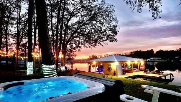 Un bain à remous et un espace extérieur aménagé avec des sièges, offrant une vue sur un bâtiment et des arbres au crépuscule.