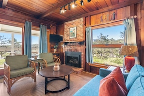 A cozy room with a fireplace, wicker furniture, and a large window with a view.