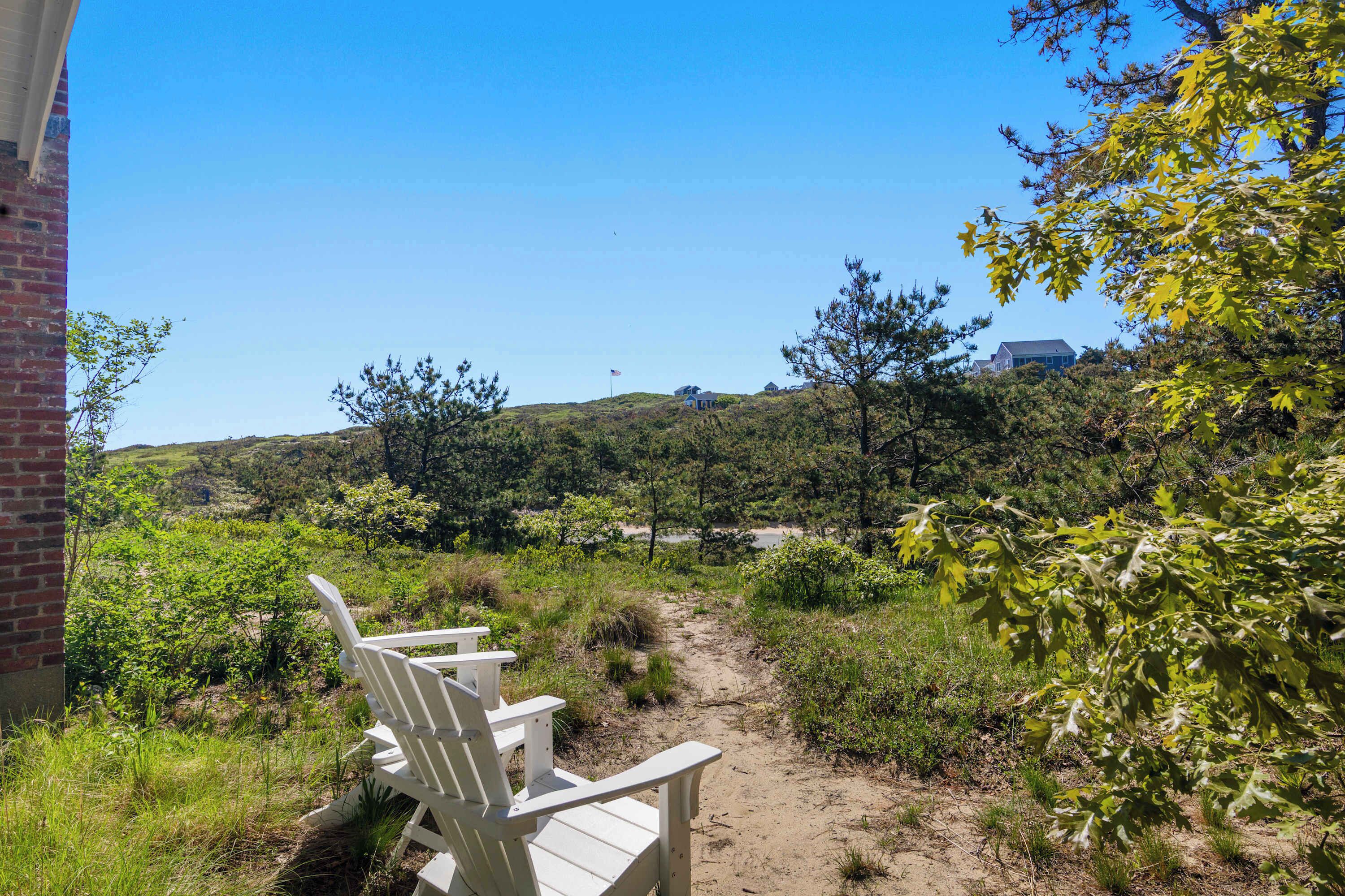 A view of a beach with a path leading to a building, surrounded by greenery and trees.