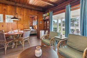 A wooden interior with wicker furniture, a dining table set with plates and glasses, and a view through a glass door.