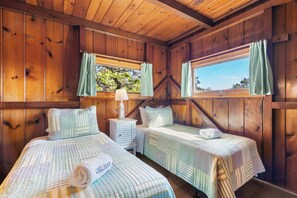 Une chambre de style cabane en bois, avec deux lits, une table de chevet, une lampe et une fenêtre avec des rideaux.