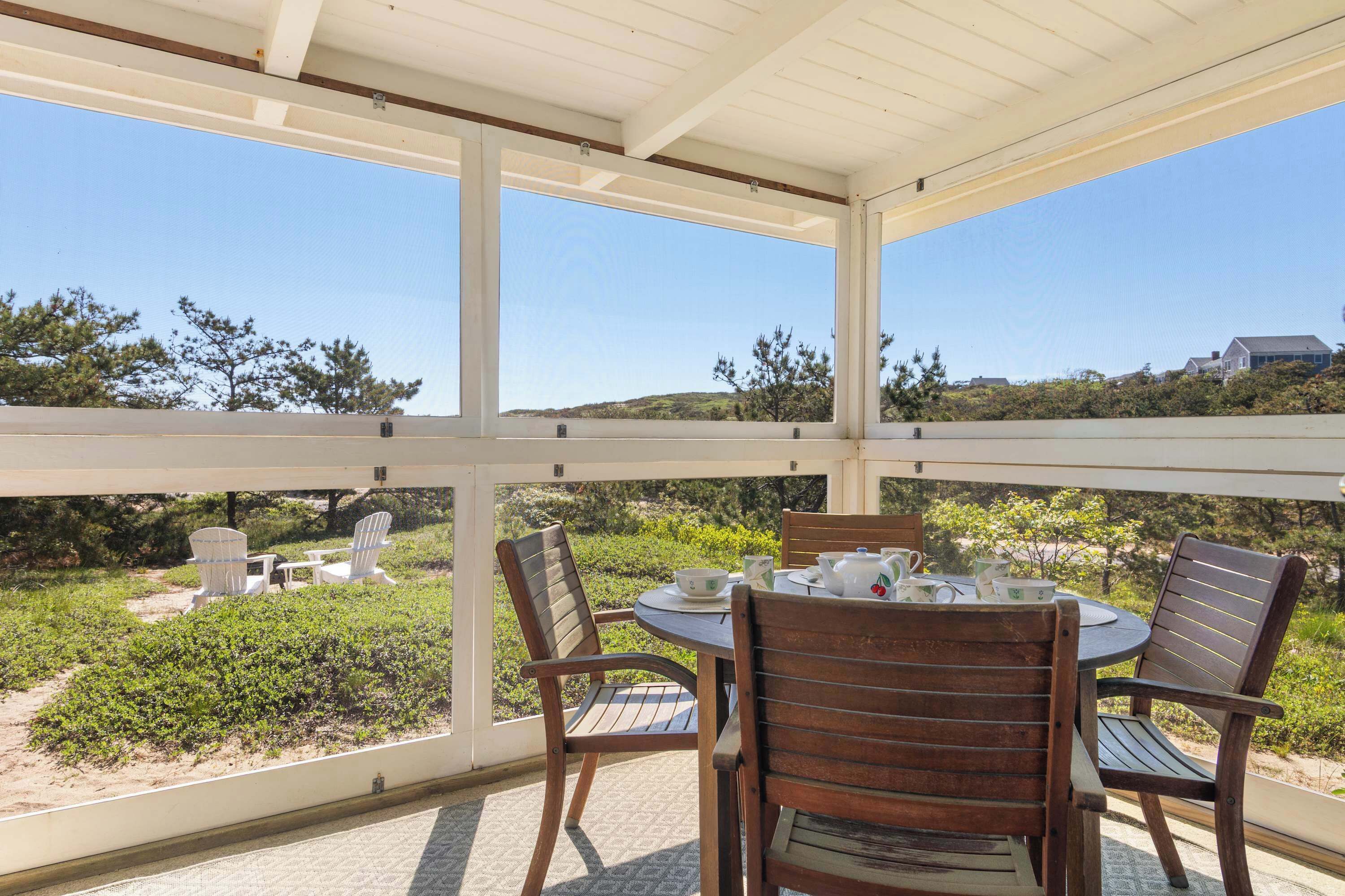 Une terrasse couverte, dotée d’une table et de chaises, qui offre une vue sur un jardin aménagé et sur des collines lointaines.