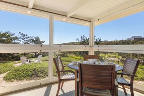 Une terrasse couverte, dotée d’une table et de chaises, qui offre une vue sur un jardin aménagé et sur des collines lointaines.
