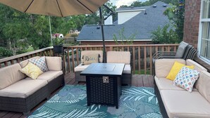 Une terrasse dotée de meubles en osier, d’une table et d’un grand parasol.