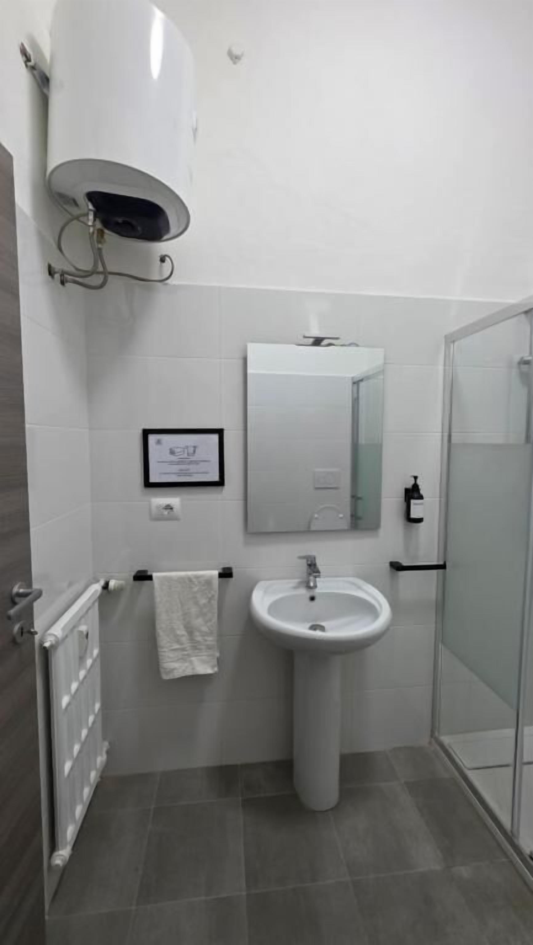 Une salle de bain comprenant un lavabo sur colonne, un miroir, un porte-serviettes, un espace douche et un radiateur.