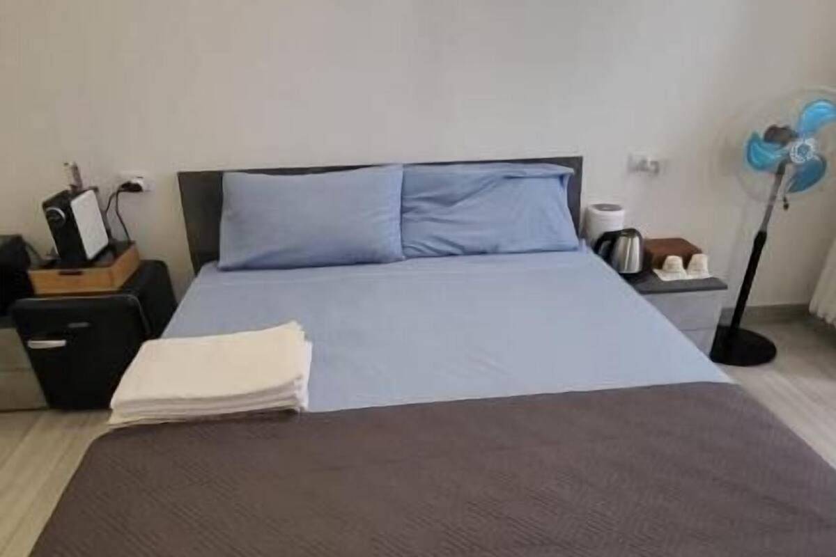 A neatly made bed with a blue and brown bedspread, a bedside table with a lamp, and a wall-mounted light fixture.