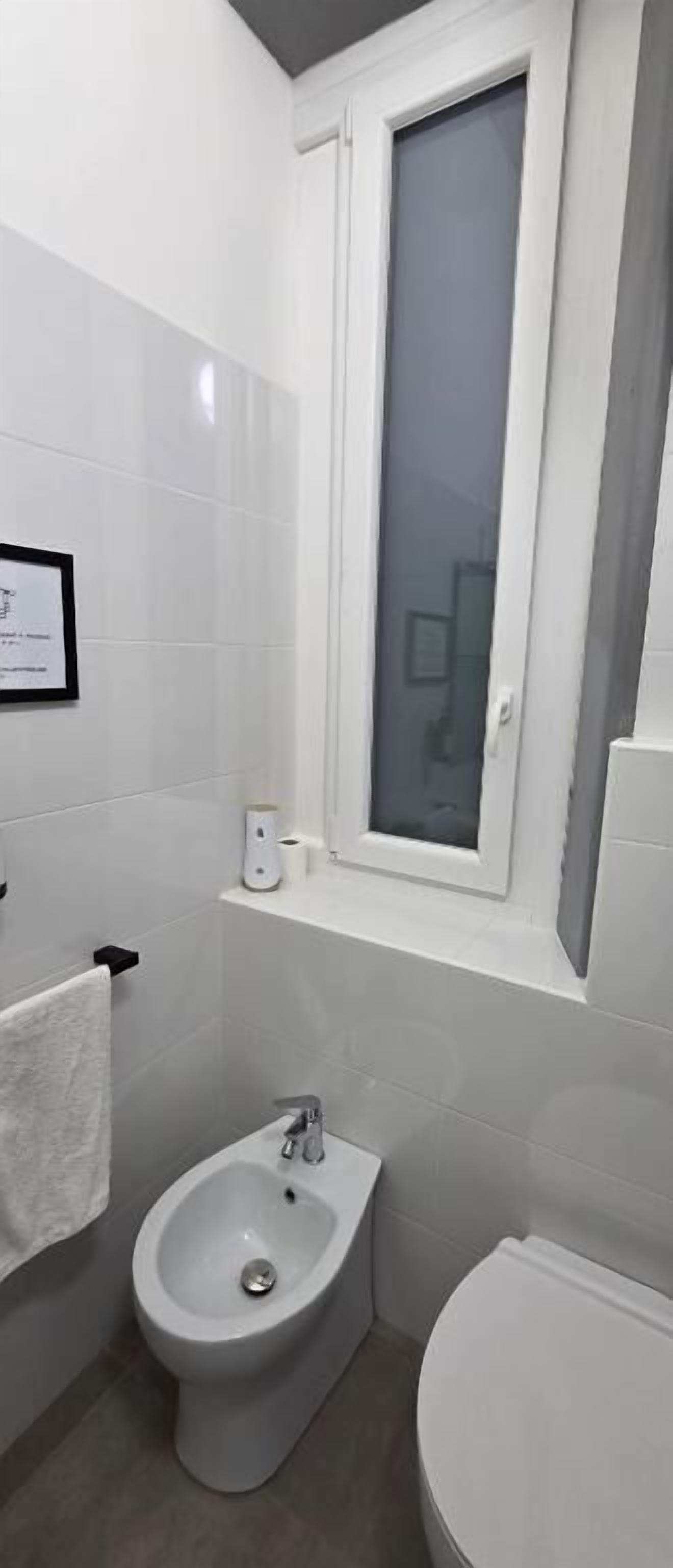 Un baño pequeño y moderno con un bidé, inodoro y una ventana sobre el inodoro.