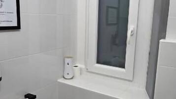 Un baño pequeño y moderno con un bidé, inodoro y una ventana sobre el inodoro.