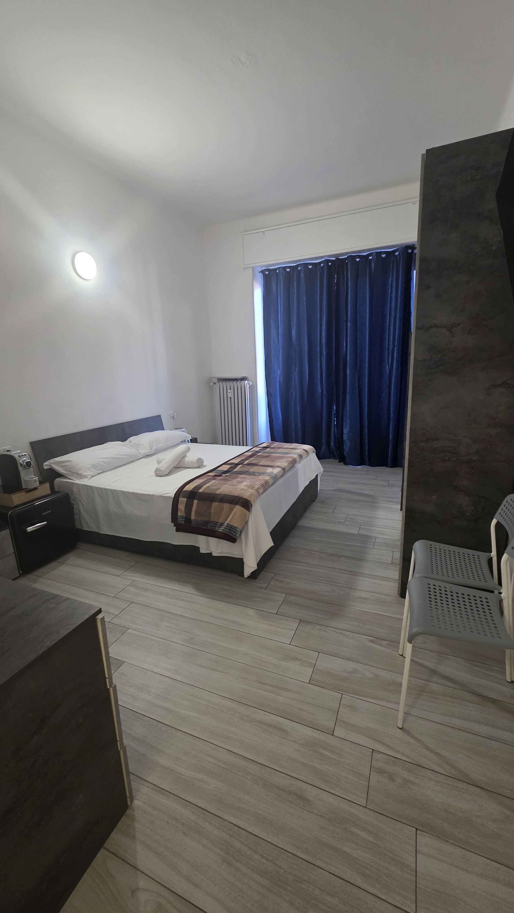Een hotelkamer met een bed, een bureau, een stoel, een radiator en een raam met gordijnen.