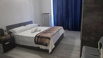 Een hotelkamer met een bed, een bureau, een stoel, een radiator en een raam met gordijnen.