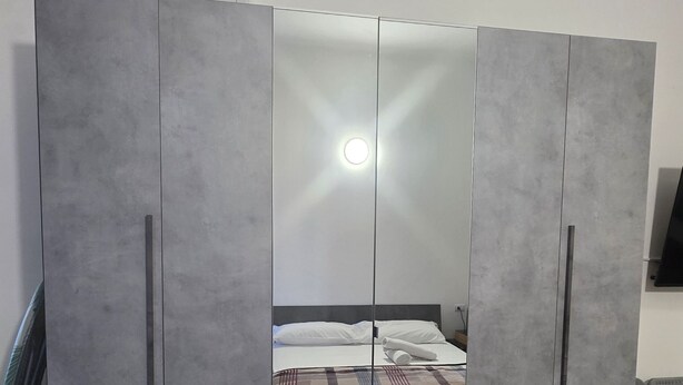 A bedroom with a bed, a wardrobe with a mirror, and a television on the wall. - Casa Manzoni (Novara)