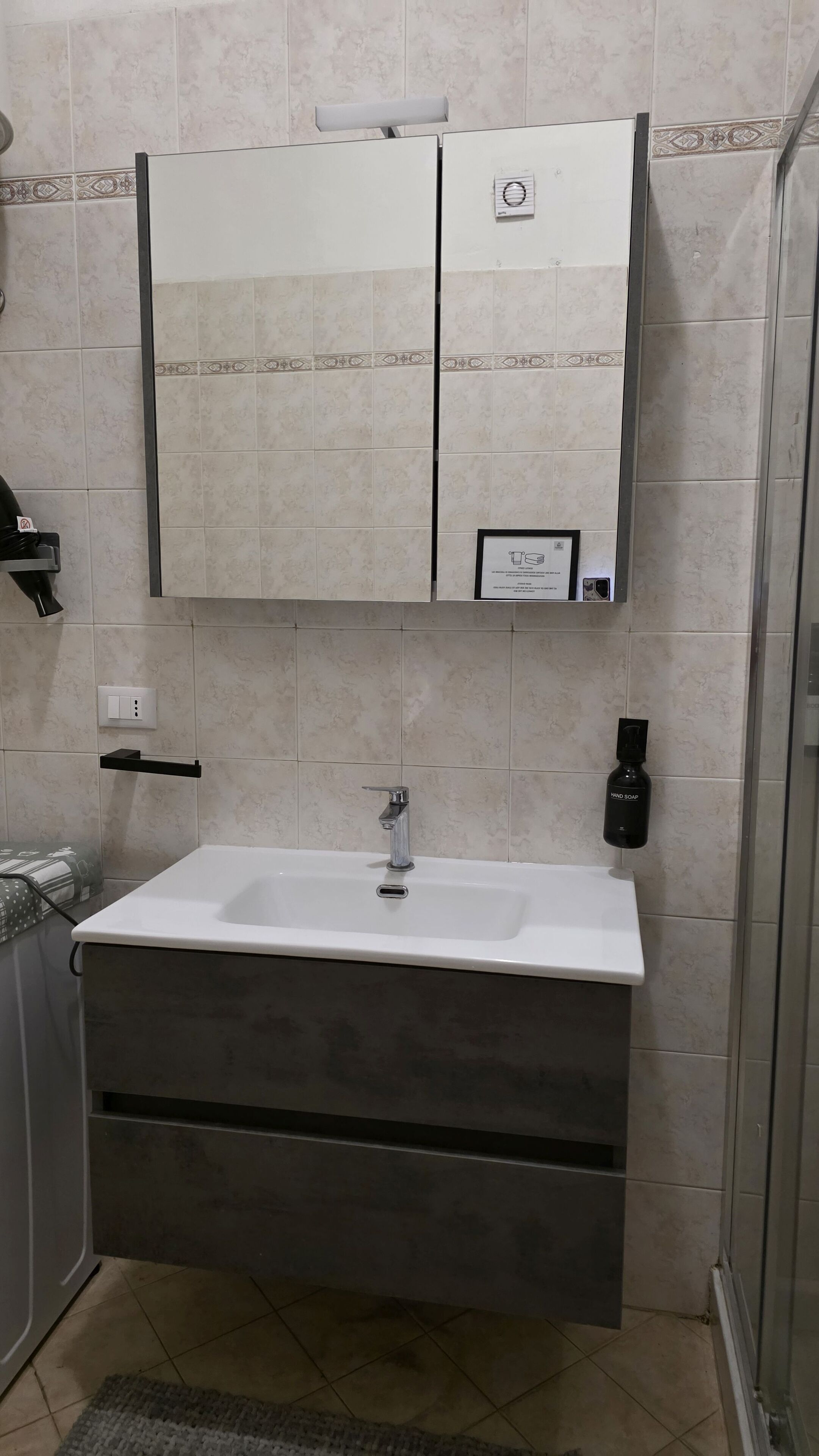 A bathroom with a white sink, a mirror above it, and a shower to the right.