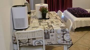 A small, cozy room with a dining table, a chair, a bed, and a radiator.