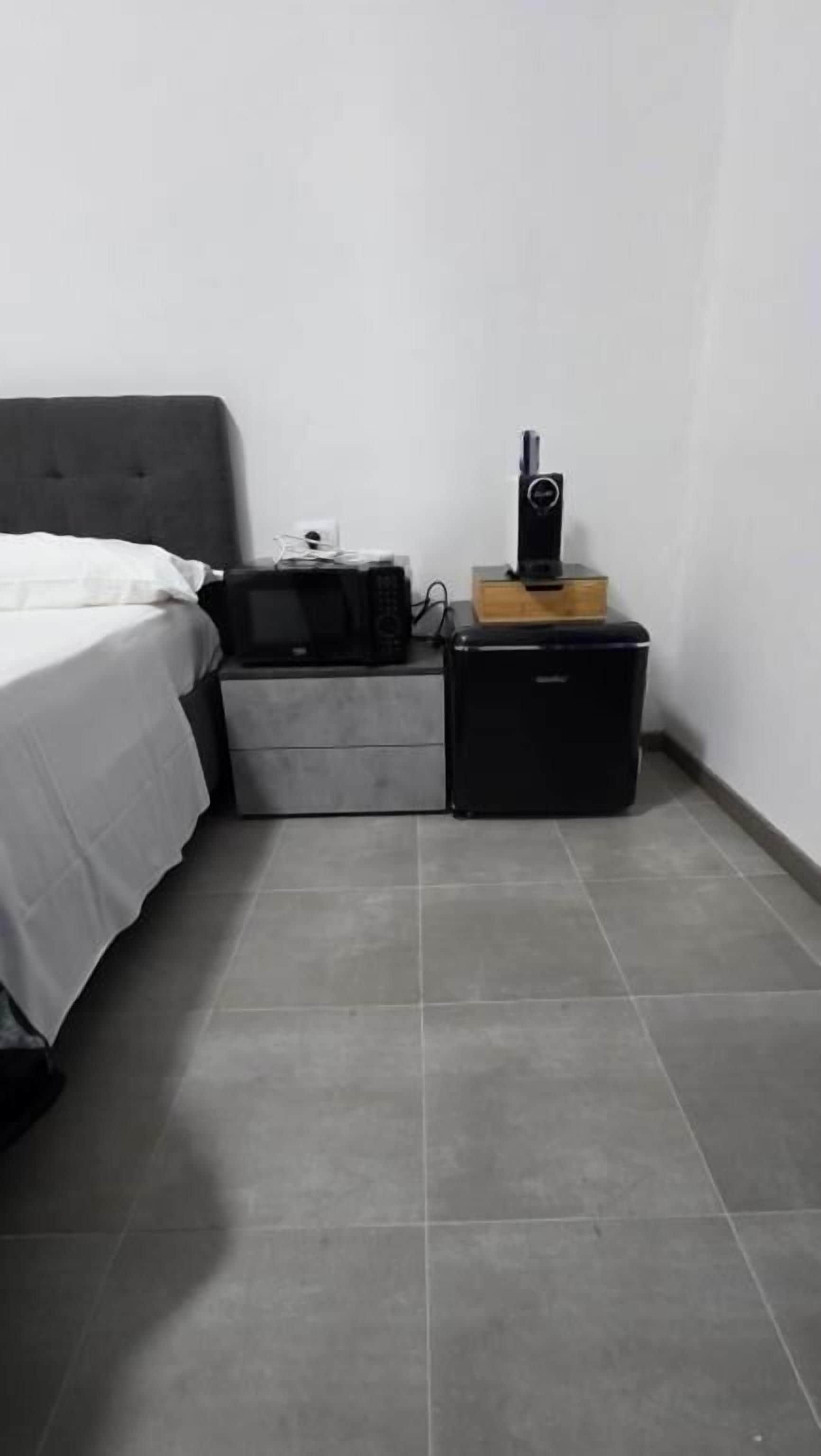 Un dormitorio con cama, mesita de noche, cómoda pequeña y altavoz.
