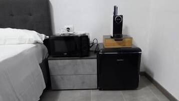 Un dormitorio con cama, mesita de noche, cómoda pequeña y altavoz.