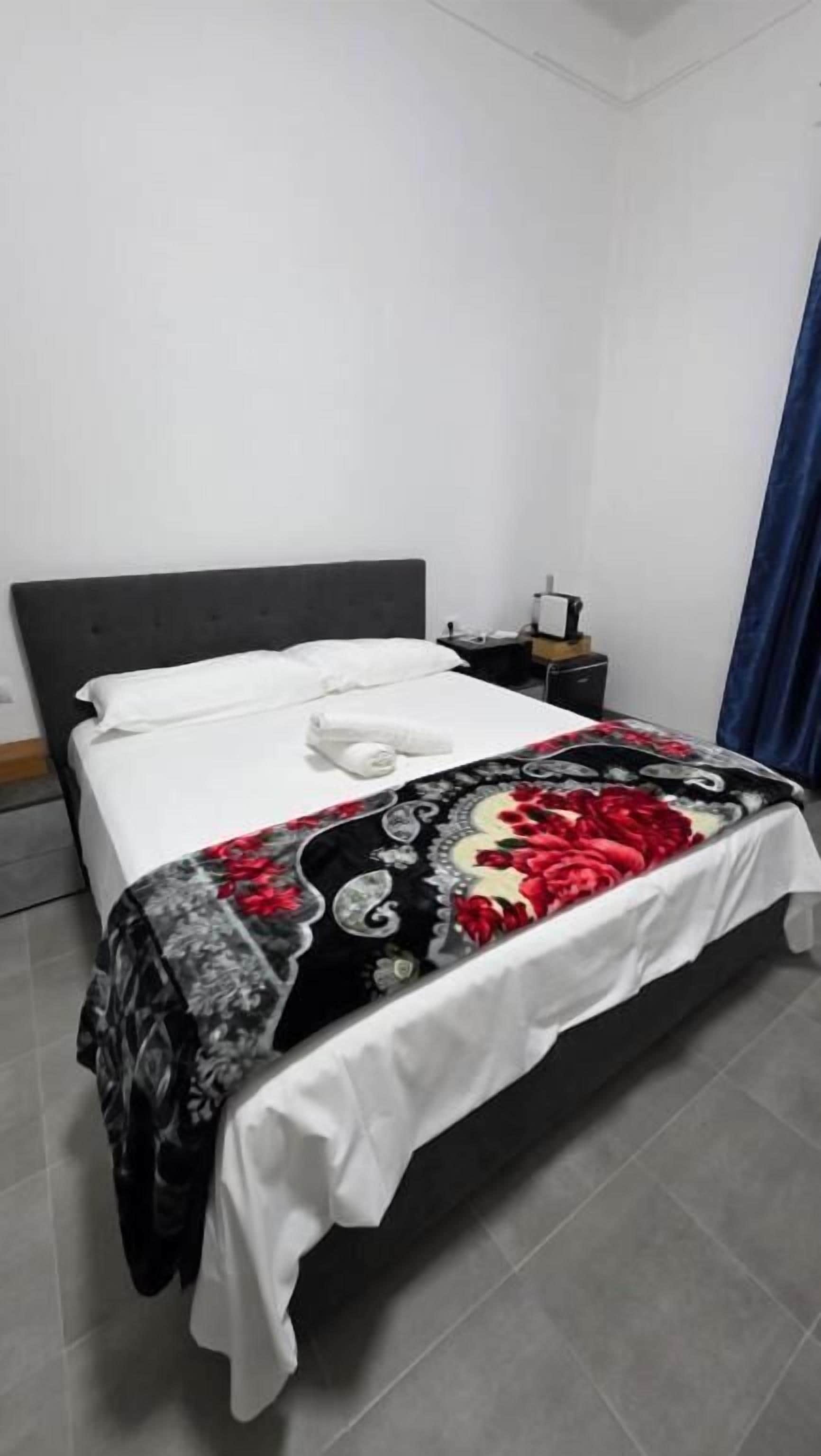 A neatly made bed with a floral bedspread, a white pillow, and a folded white towel.