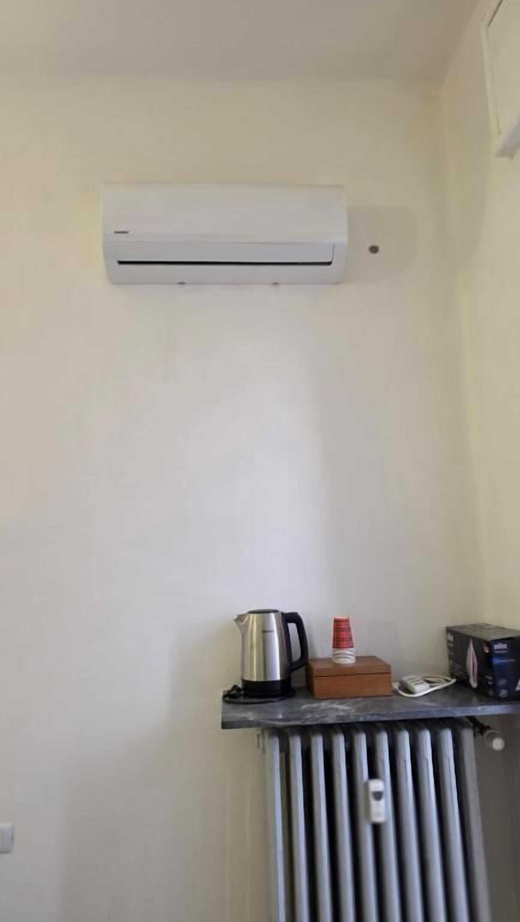 Una kitchenette pequeña con aire acondicionado integrado, un hervidor, una cafetera y una caja de pañuelos sobre una encimera.