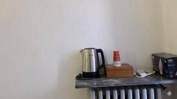 Una kitchenette pequeña con aire acondicionado integrado, un hervidor, una cafetera y una caja de pañuelos sobre una encimera.