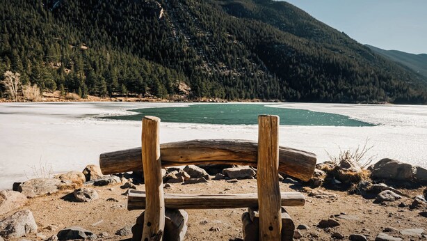 Un banc en bois donnant sur un lac gelé, avec des montagnes en arrière-plan.