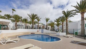 A swimming pool with lounge chairs, palm trees, and a white building with a tiled roof.