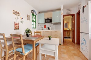 Une cuisine compacte dotée d’appareils électroménagers modernes, un coin repas avec des chaises et une table en bois, et un couloir menant à l’espace de vie.