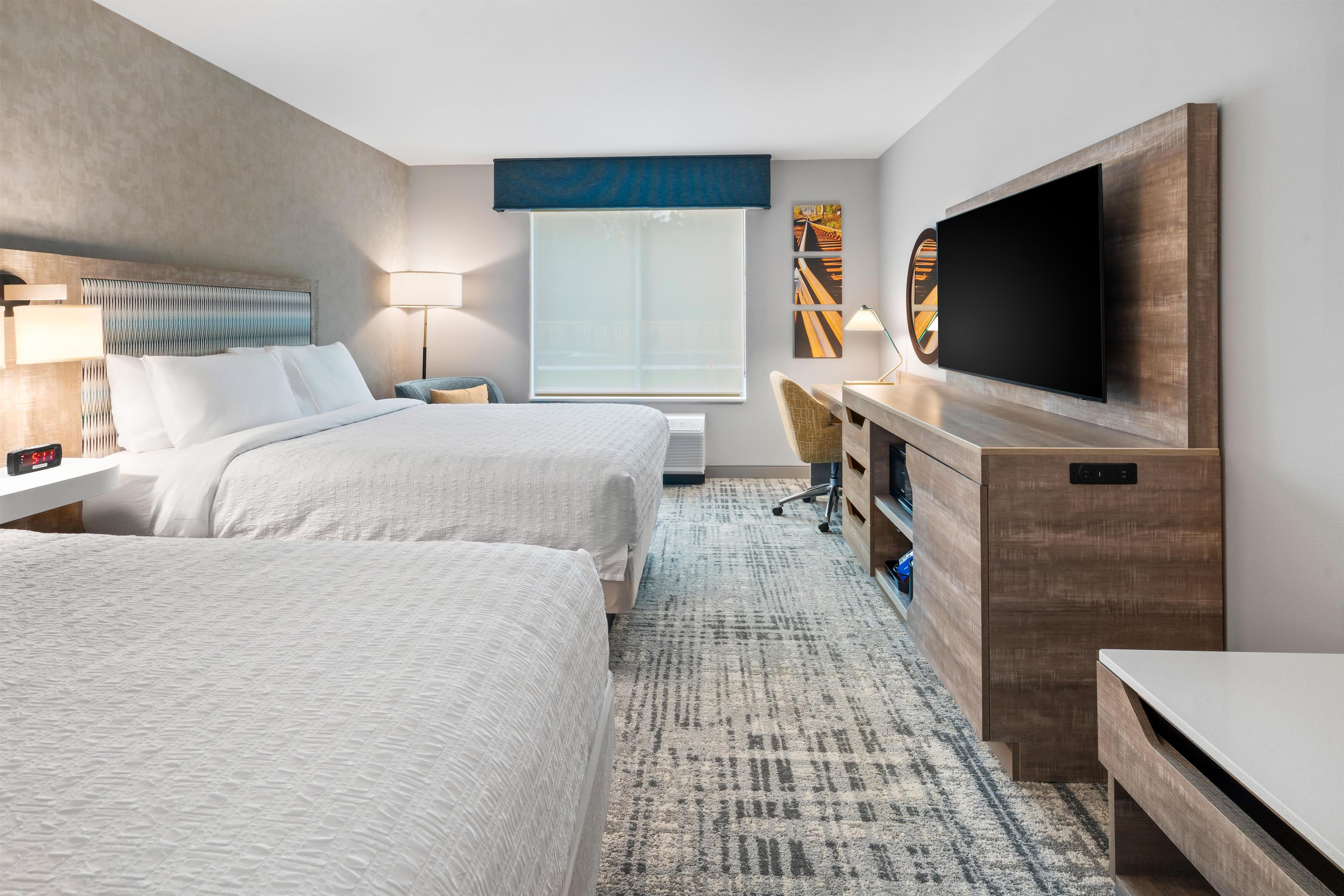 Une chambre d’hôtel avec deux lits, un bureau, une télévision et une grande fenêtre.