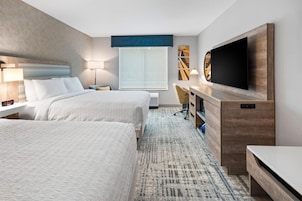 A hotel room with two beds, a desk, a TV, and a large window.