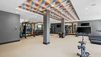 A gym with exercise equipment, a treadmill, and a colorful ceiling design.