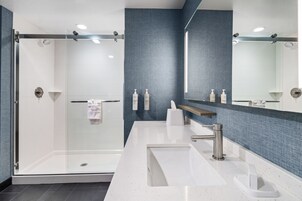 A modern bathroom with a glass shower enclosure, a white sink with a mirror above it, and a blue textured wall.
