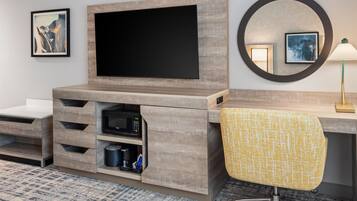 Ein Hotelzimmer mit Flachbildfernseher an einer Holzeinrichtung, einer Mikrowelle, einer Kaffeemaschine und einem Sessel mit gelbem Kissen.