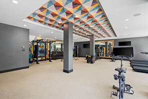 Un gimnasio con equipo de ejercicio, una bicicleta estática y un techo con un estampado geométrico colorido.