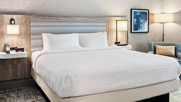 A hotel room with a large bed, a nightstand with a lamp, a wall-mounted clock, and a framed picture on the wall.