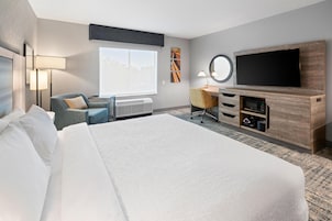 Quarto de hotel com uma cama grande, escrivaninha, televisão de tela plana e janela com vista.