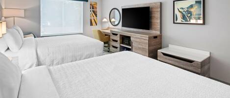 A hotel room with two beds, a desk, a flat-screen TV, a mirror, and artwork on the walls.