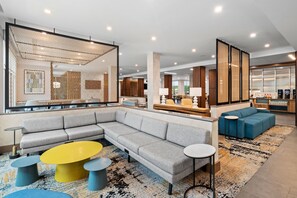 A modern hotel lobby with a large sectional sofa, a coffee station, and a seating area with a blue sofa and round tables. - Hampton Inn By Hilton Aiken (Aiken)
