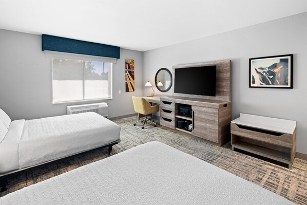 Una habitación de hotel con cama, escritorio, televisor y ventana.