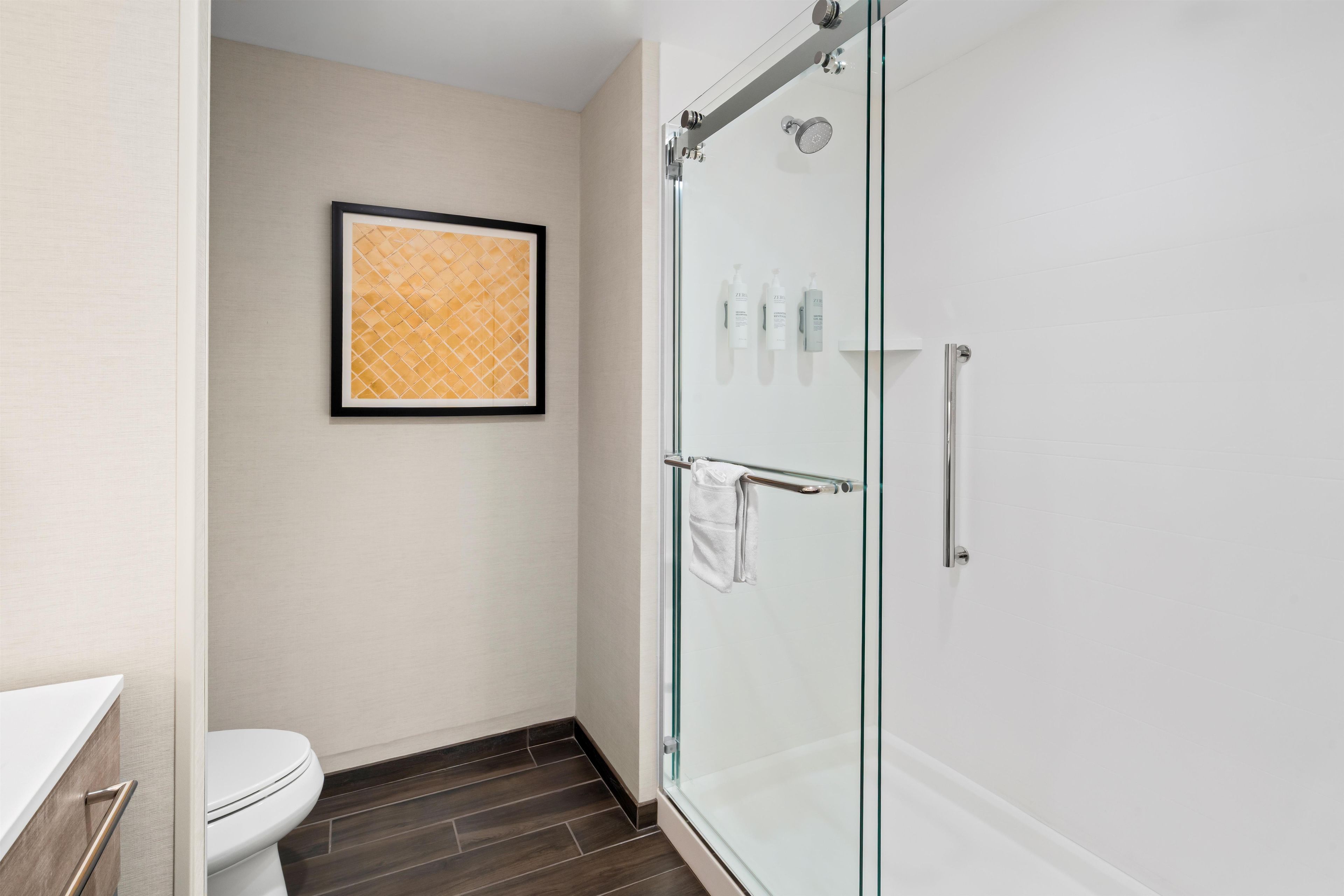 A modern bathroom with a glass shower enclosure, a toilet, and a framed artwork on the wall.