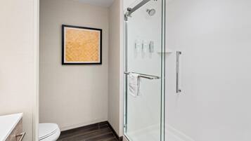 Een moderne badkamer met een douchecabine van glas, een toilet en een kunstwerk in een lijst aan de muur.