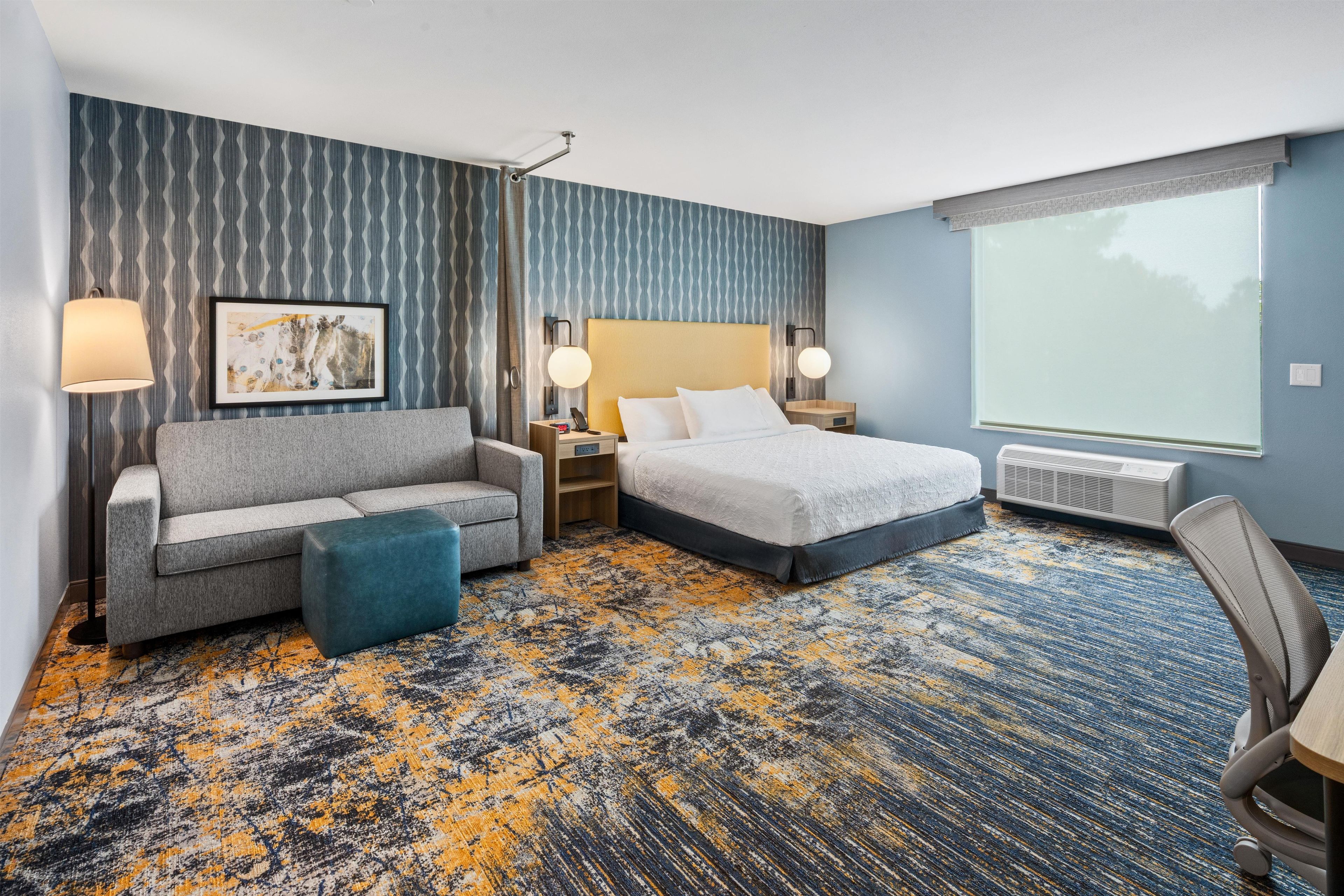 A hotel room with a bed, a sofa, a desk, a chair, and a large window.