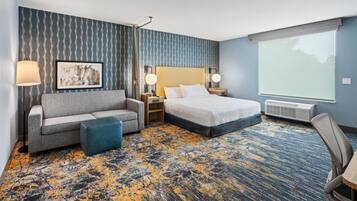 A hotel room with a bed, a sofa, a desk, a chair, and a large window.