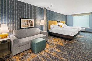 Een hotelkamer met een bank, een bed, een kleine tafel, een lamp en een schilderij aan de muur.