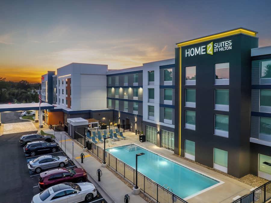 A hotel with a swimming pool, multiple parking spaces, and a clear sky.