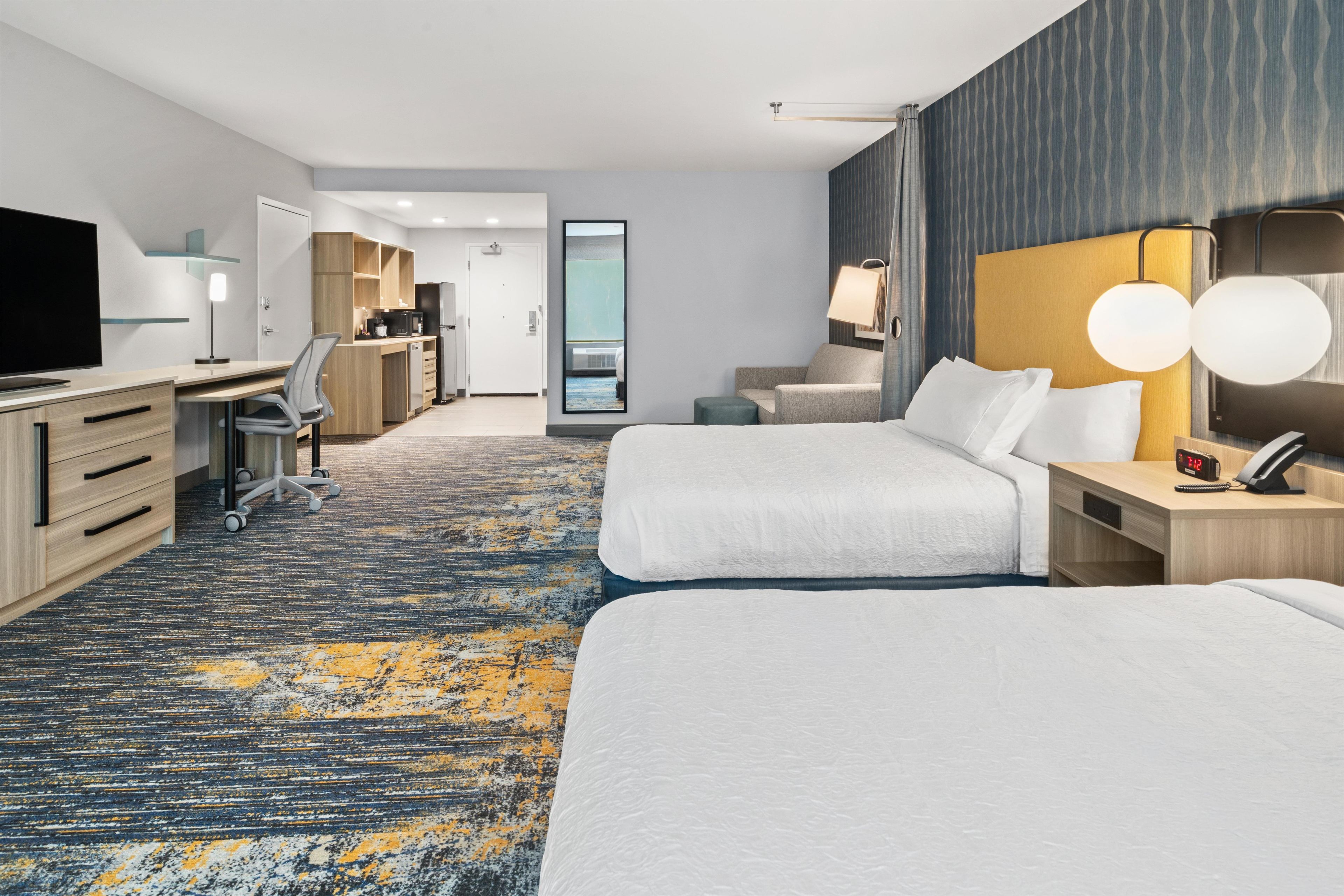 A hotel room with two beds, a desk, a chair, a television, and a bathroom visible through a door.