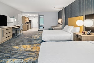 Habitación de hotel con dos camas, un escritorio, una silla, un televisor y un baño visible a través de una puerta.