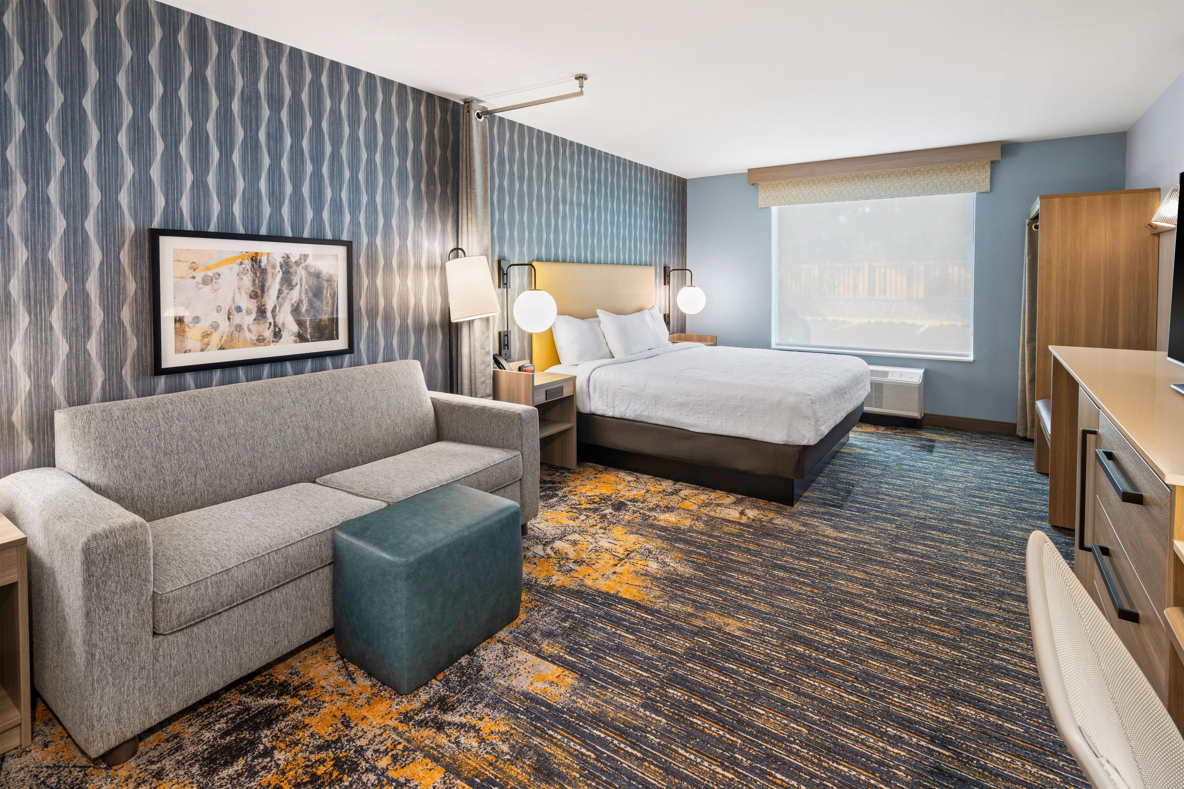 A hotel room with a sofa, a bed, a desk, and a large window.