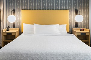 Una habitación de hotel con una cama grande, dos mesitas de noche, un cabecero de madera y lámparas fijadas a la pared.